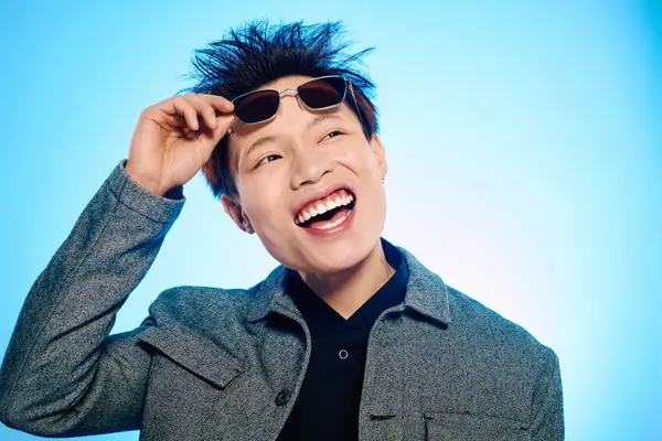A young man with a trendy outfit joyfully adjusts his sunglasses while beaming a bright smile. — Stock Photo