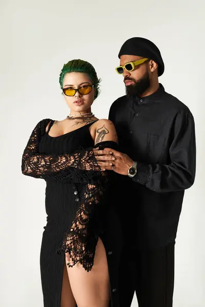 Um casal na moda posa confiantemente em um estúdio, exibindo suas roupas elegantes e óculos de sol. — Fotografia de Stock