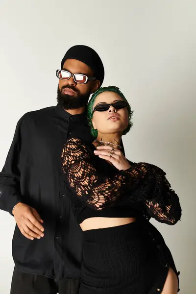 Una pareja joven y elegante posa con confianza en un estudio brillante, con gafas de sol. - foto de stock
