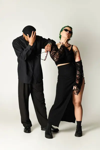 Couple strikes a confident pose, showcasing unique styles and sunglasses in a modern studio. — Stock Photo