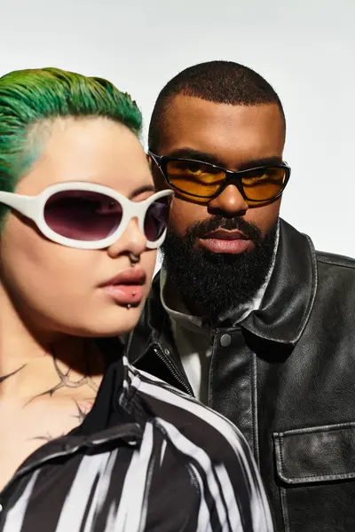 A fashionable couple showcases their unique styles in a studio, wearing bold sunglasses. — Stock Photo