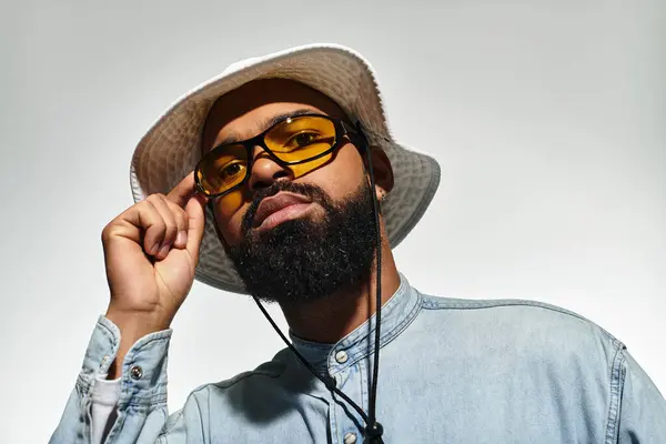 A stylish Black man in sunglasses and a sun hat exudes confidence in a bright studio. — Stock Photo