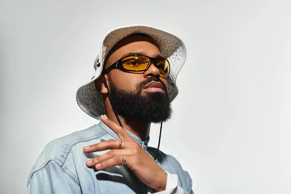 A fashionable young African American man poses confidently in a studio, wearing stylish sunglasses and a sun hat. — Stock Photo