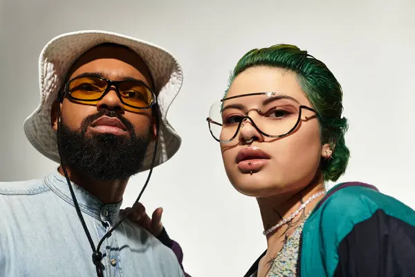 A stylish couple with diverse backgrounds poses confidently in a studio, wearing bold sunglasses. — Stock Photo