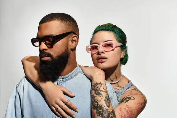 A stylish couple poses confidently, showcasing trendy sunglasses and vibrant outfits in a studio. — Stock Photo