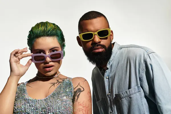 A trendy couple models their stylish outfits and sunglasses against a modern backdrop. — Stock Photo