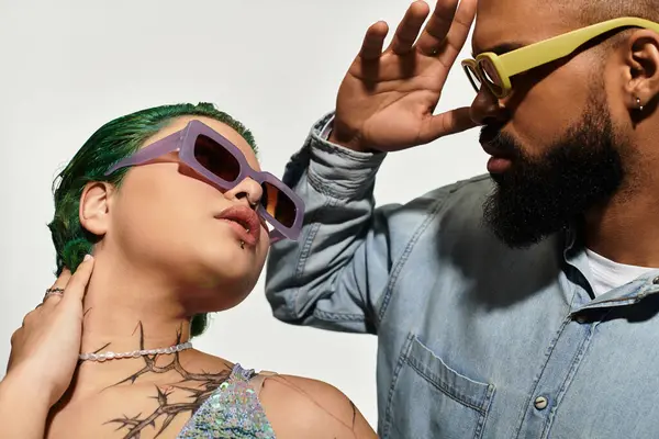Young couple showcases their stylish outfits and sunglasses in a vibrant studio setting. — Stock Photo