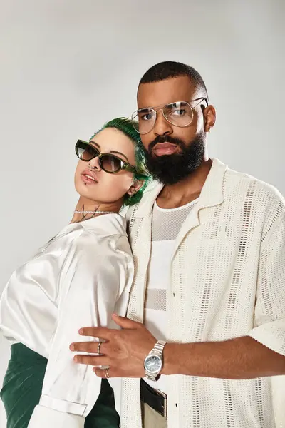 Multicultural duo confidently showcases unique styles and sunglasses in a trendy studio. — Stock Photo