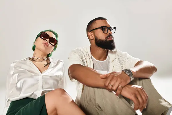 A fashionable couple poses confidently in a studio, radiating style and diversity with sunglasses. — Stock Photo