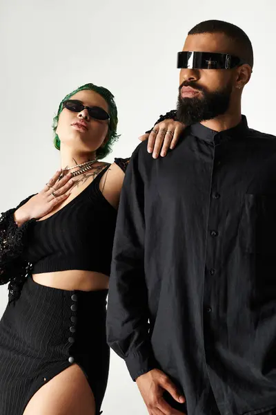 Una joven pareja multicultural posa con confianza en trajes de moda mientras usa gafas de sol. - foto de stock