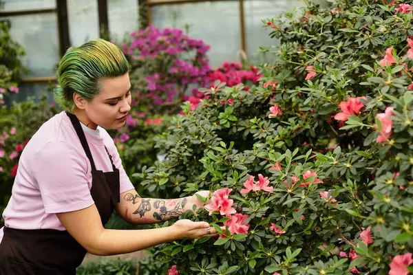 A young woman carefully examines colorful flowers while working in a vibrant greenhouse setting. — Stock Photo
