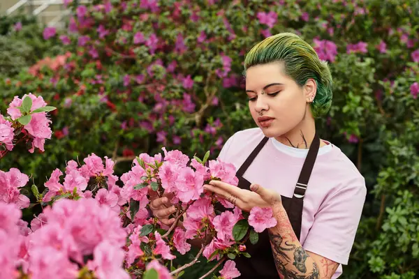 In a green house, a young woman tends to blooming pink flowers, enjoying natures beauty. — Stock Photo