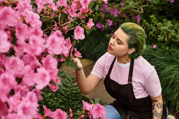 Uma jovem examina cuidadosamente flores rosa florescendo enquanto trabalha em uma estufa exuberante. — Fotografia de Stock