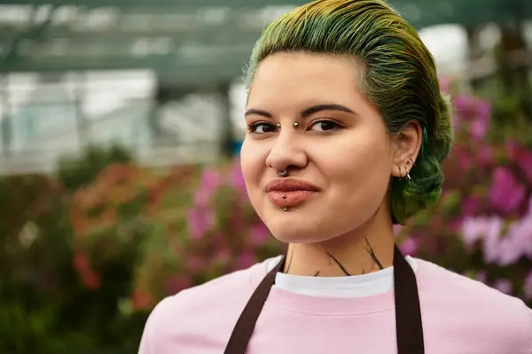 In a vibrant greenhouse, a young woman with colorful hair smiles while tending to plants. — Stock Photo