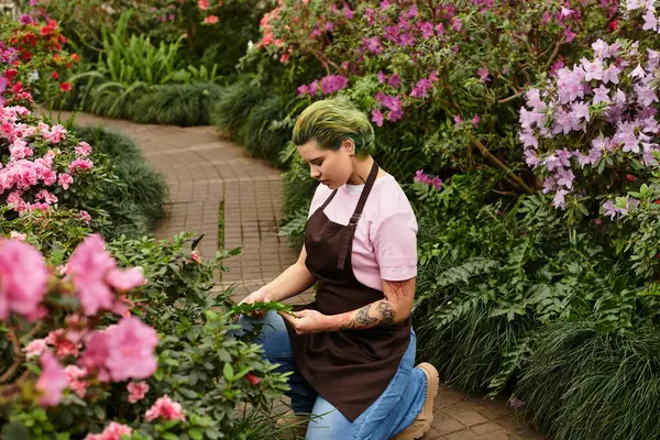 Focused woman nurtures green plants in a lively greenhouse filled with blooming flowers. — Stock Photo