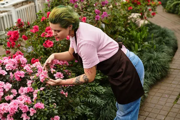 A young woman in a pink shirt tends flowers in a lush greenhouse full of greenery. — Stock Photo