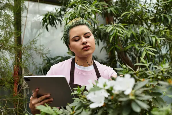 Dans une serre vibrante, la jeune femme interagit avec les plantes à l'aide de sa tablette. — Photo de stock