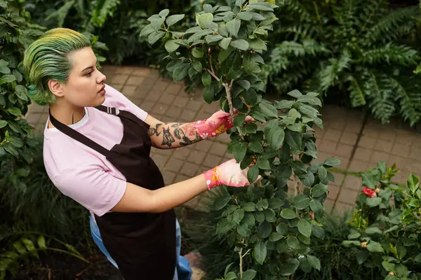 Una joven con el pelo verde poda cuidadosamente las plantas mientras se dedica a sus tareas de jardinería. - foto de stock