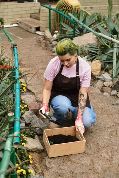 A young woman diligently cultivates soil in a lively greenhouse, surrounded by blooming plants. — Stock Photo