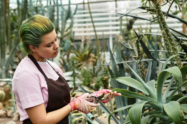 Une jeune femme taille soigneusement les plantes dans une serre animée remplie de verdure. — Photo de stock