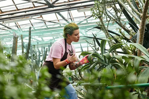 Une jeune femme aux cheveux verts nourrit des plantes dans une serre, concentrée sur sa tâche de jardinage. — Photo de stock
