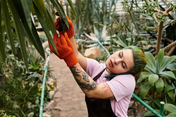 A young woman attends to plants in a lively greenhouse, showcasing her dedication and passion. — Stock Photo