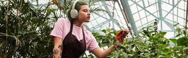 In a lush greenhouse, a young woman carefully nurtures green plants while listening to music. — Stock Photo