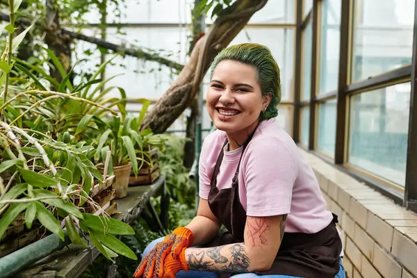 A smiling woman tends to plants in a cozy greenhouse filled with bright colors. — Stock Photo