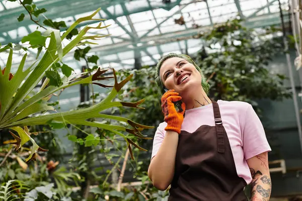 Engaging in plant care, the young woman smiles brightly while communicating on her phone. — Stock Photo