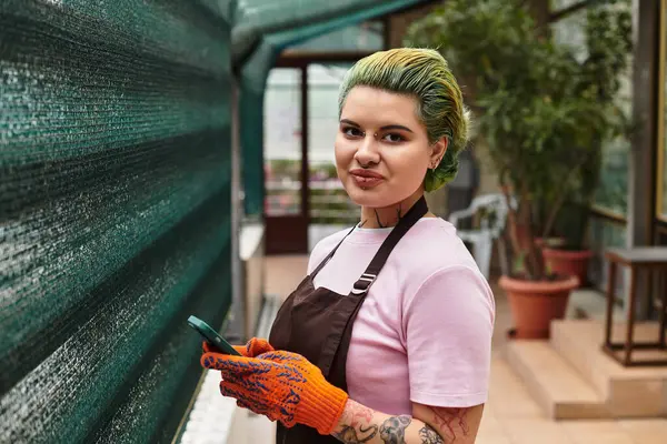 Engaged in gardening, a young woman with green hair enjoys her work in a bright greenhouse. — Stock Photo