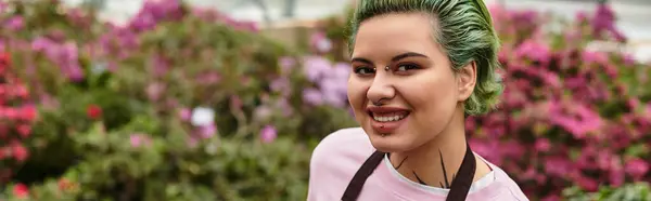 Entusiasta joven mujer nutre verdor en un animado invernadero lleno de flores de colores. — Stock Photo