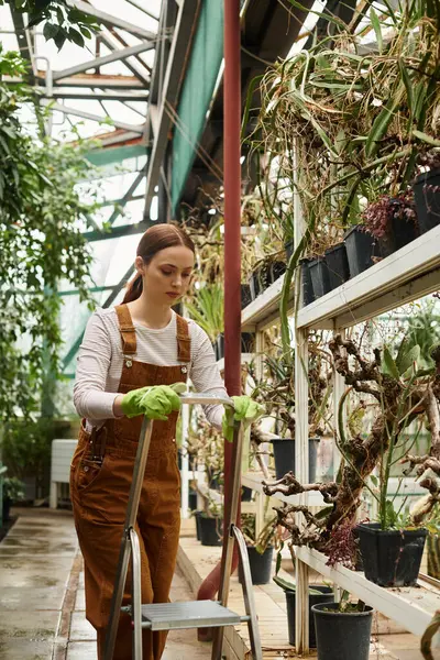 En un invernadero vibrante, una joven poda cuidadosamente las plantas mientras está rodeada de exuberante follaje. - foto de stock
