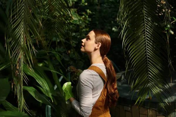 Beautiful young woman enjoys the peaceful atmosphere in a lush greenhouse surrounded by greenery. — Stock Photo