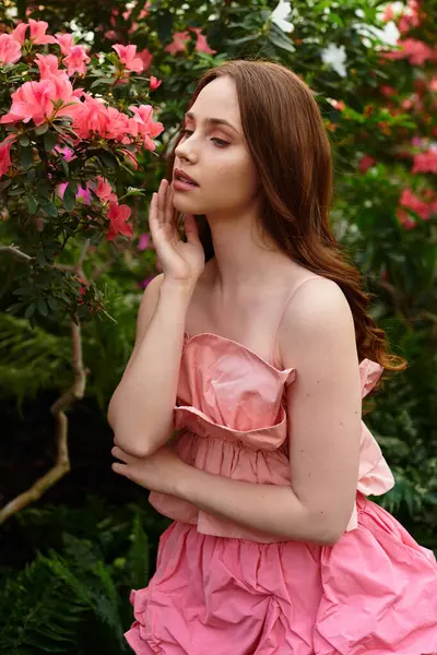 In a lush greenhouse, a young beautiful woman gently touches blooming flowers, immersed in nature. — Stock Photo