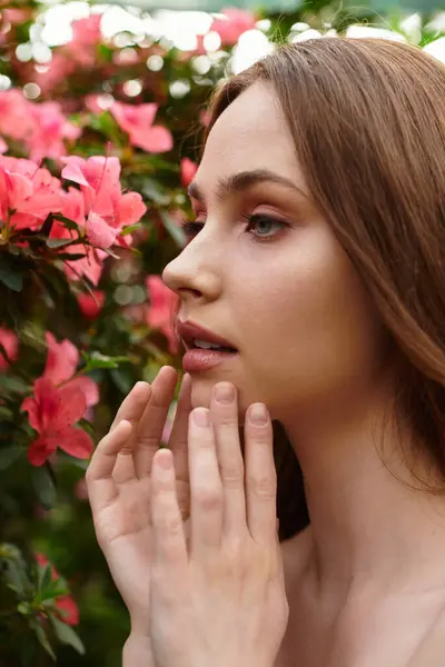 A lovely young woman softly touches her face amid vibrant flowers in a greenhouse. — Stock Photo