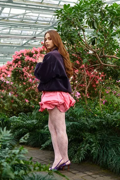 Beautiful woman stands gracefully among vibrant flowers in a tranquil greenhouse setting. — Stock Photo