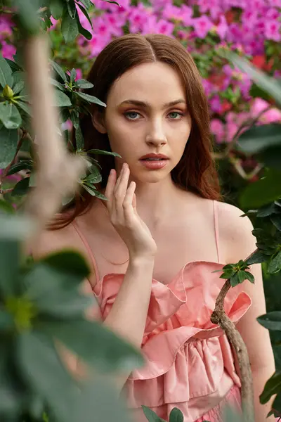 Una joven mujer delicadamente toca su cara en medio de una exuberante vegetación y flores florecientes. - foto de stock