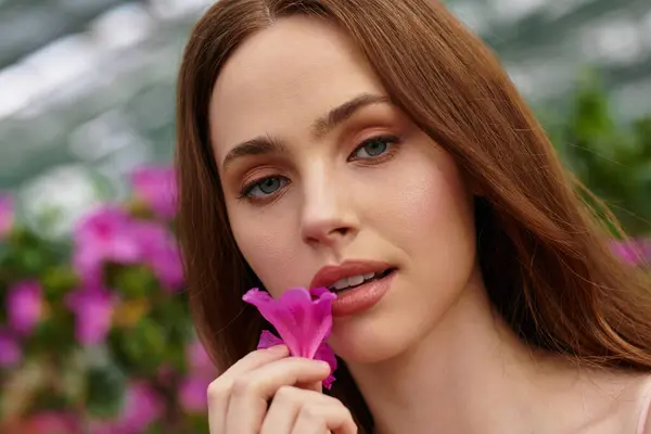 A young woman gently touches a pink flower, enjoying the tranquility of the greenhouse. — Stock Photo