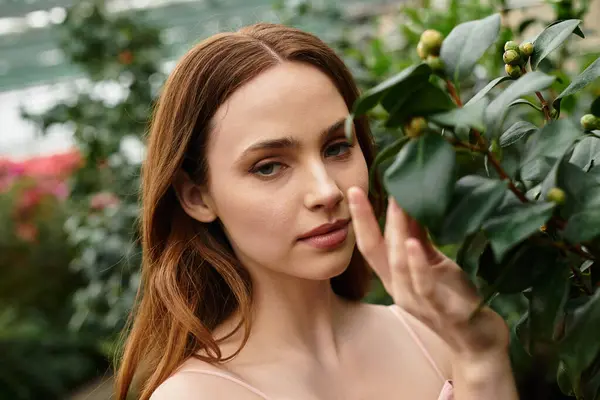 A young woman gently touches a leafy plant in a vibrant greenhouse. — Stock Photo