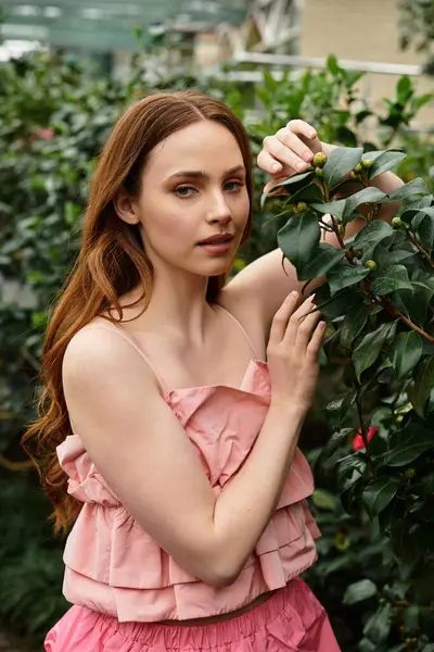 A young beautiful woman gently touches a green plant in a vibrant greenhouse filled with life. — Stock Photo