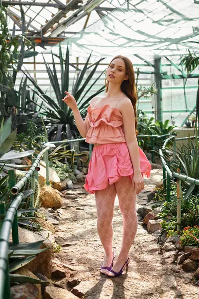Woman gracefully poses in a greenhouse, highlighting her playful outfit and beauty. — Stock Photo