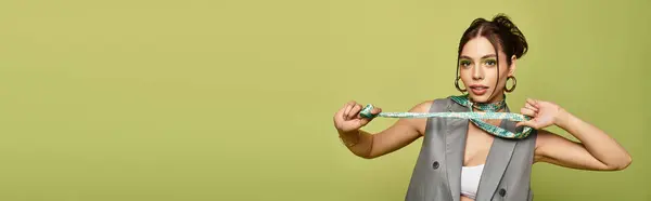 A young woman displays her unique style, playfully holding a scarf against a green wall. — Stock Photo