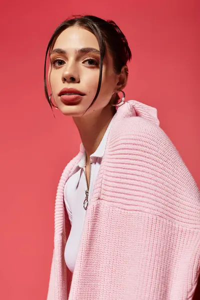 A young beautiful woman elegantly poses in a cozy pink sweater, radiating confidence and charm. — Stock Photo