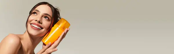 Uma jovem alegre brinca com um recipiente laranja no rosto, sorrindo brilhantemente. — Fotografia de Stock