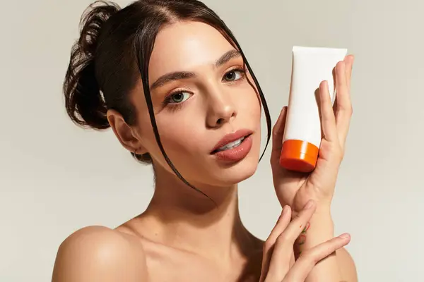 Young woman flaunts skincare cream against a neutral backdrop, radiating confidence and grace. — Stock Photo