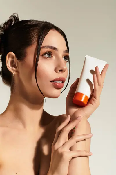 A confident young woman holds a skincare tube to her face, enjoying the natural light. — Stock Photo