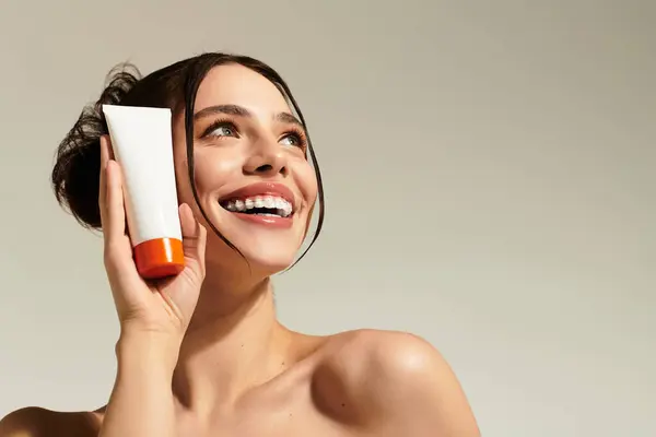 Young woman showcases a skincare product while smiling brightly in a cheerful atmosphere. — Stock Photo