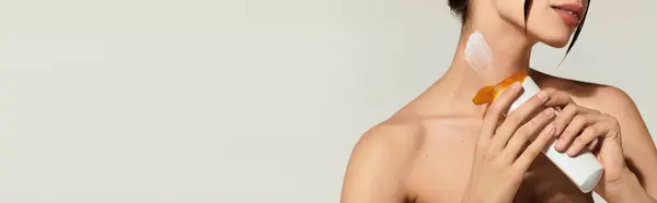 Une jeune femme applique une lotion sur son cou, soulignant sa routine de soins de la peau dans un cadre calme. — Photo de stock