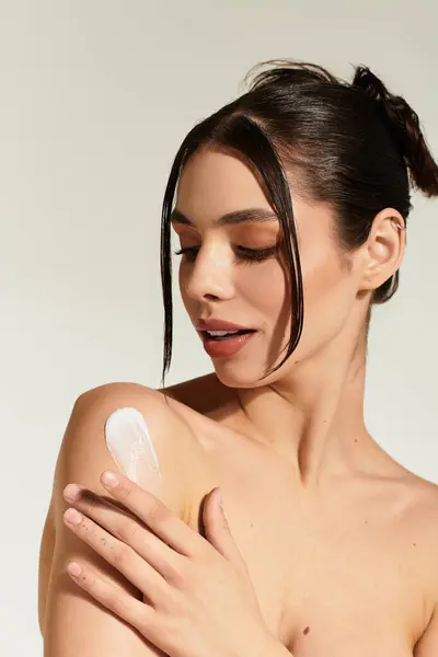 Young woman applies lotion to her shoulder, revealing radiant skin and elegance. — Stock Photo