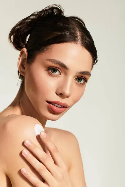 A young woman applies lotion on her shoulder, savoring a moment of elegant self care. — Stock Photo